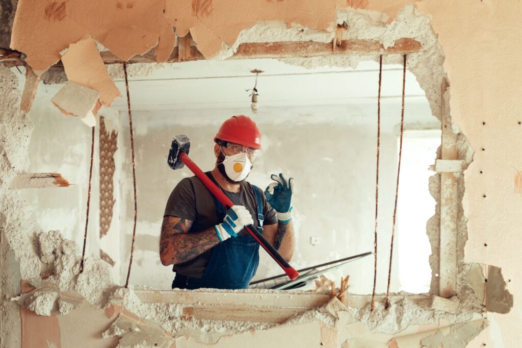A man in a hard hat and safety glasses holding a hammer during interior demolition process.