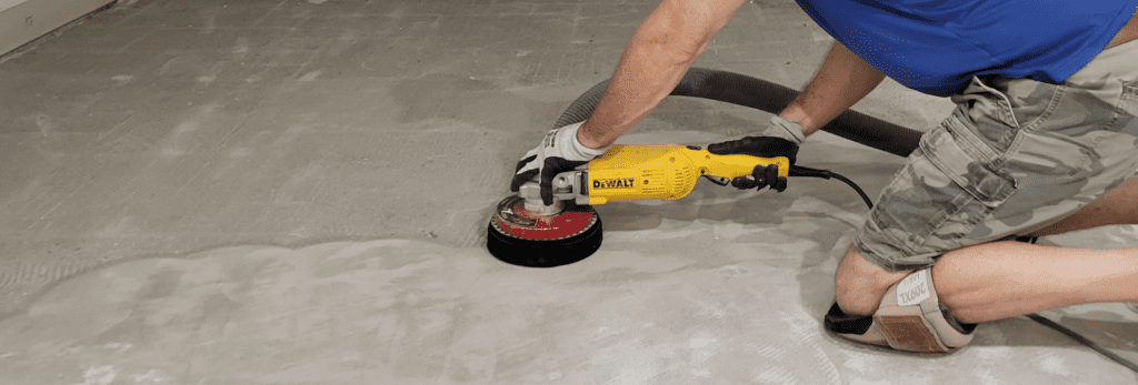 A man is using a sander to refine the texture of concrete, demonstrating a skilled approach to surface preparation.