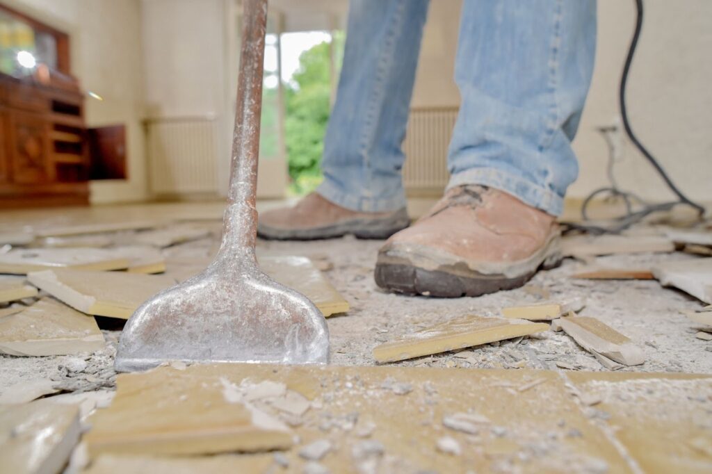 Worker using a crowbar to remove floor tiles in a room.