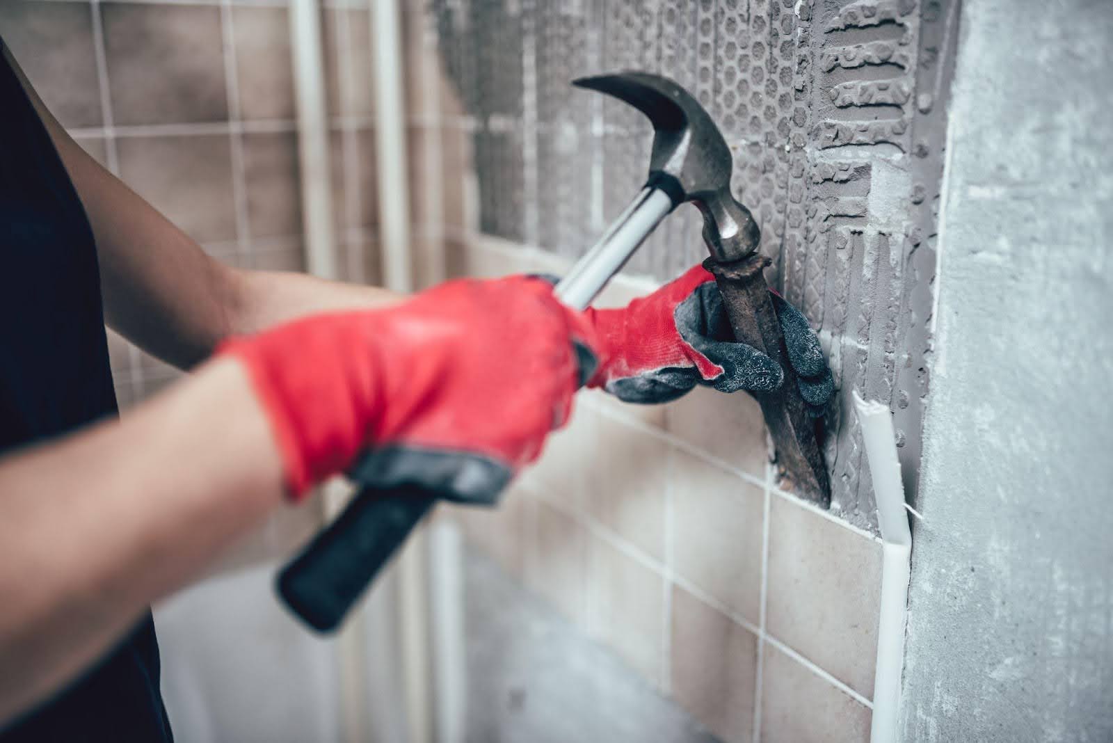 A hand in a red glove grips a hammer indicating preparation for a construction or repair activity