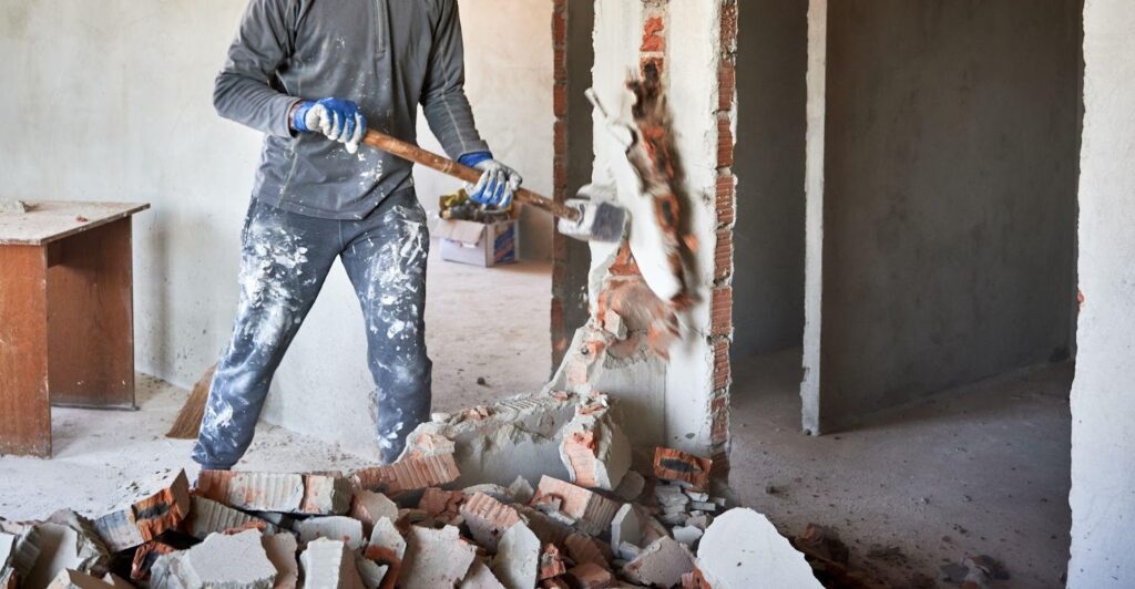 A man strikes a wall with a hammer actively engaged in demolition or remodeling tasks