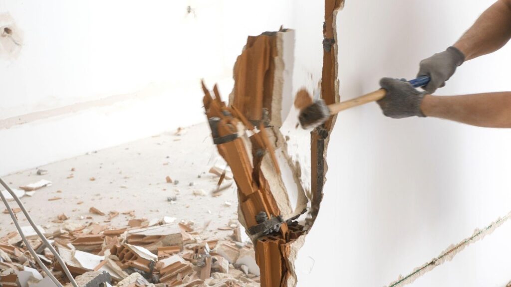 A man uses a hammer to remove wooden planks from a wall during a renovation project
