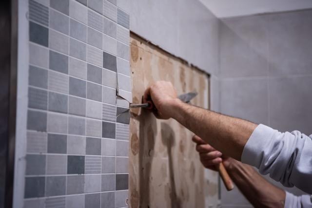 A man works on installing tiles in a bathroom focusing on precision with a set of tools at his side