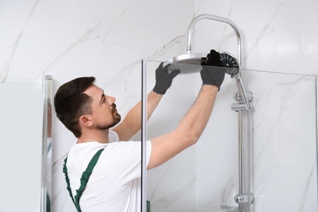A man in a white shirt and black gloves is repairing a shower head in a bathroom setting