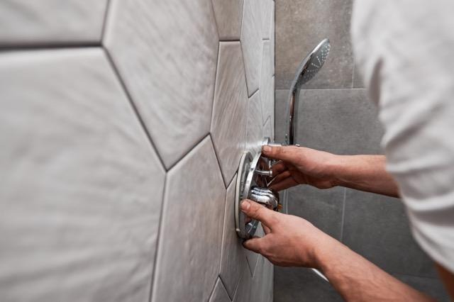 A man is adjusting a shower head on a wall focused on fixing it securely in place