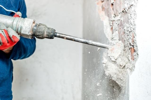 A man uses a power drill to take down part of a wall during a renovation project
