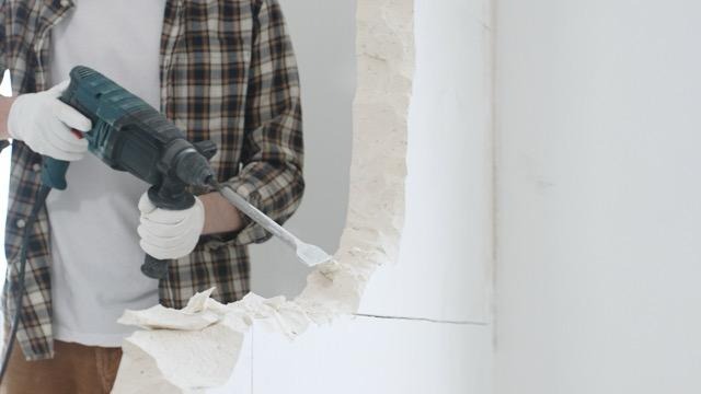 A man repairs a wall using a drill focused on his task in a well-lit room