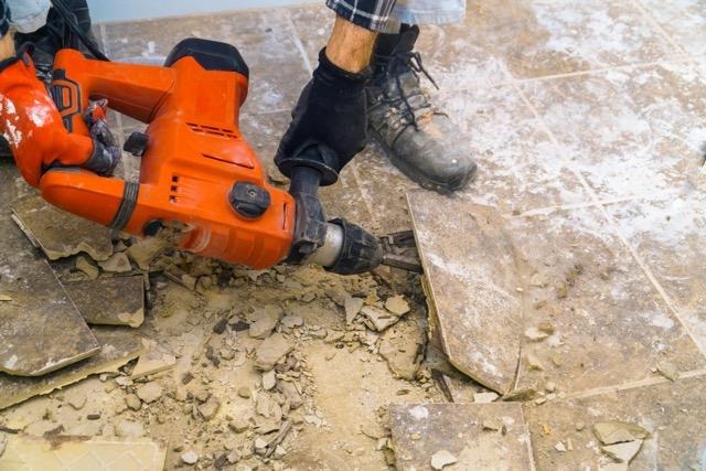 A man repairs a tile floor using an electric drill focused on his task in a well-lit room