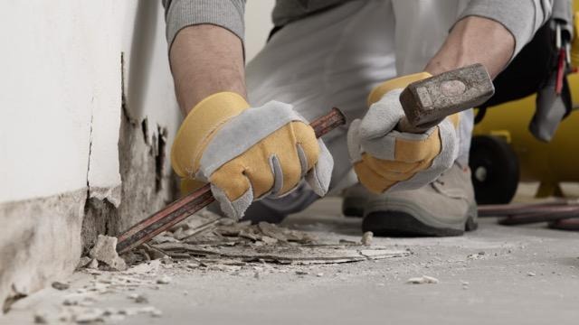 A man wearing gloves holds a hammer showcasing a yellow glove on his hand ready for a task