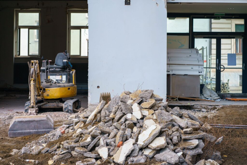 A small yellow excavator next to a pile of concrete rubble inside a building under renovation.
