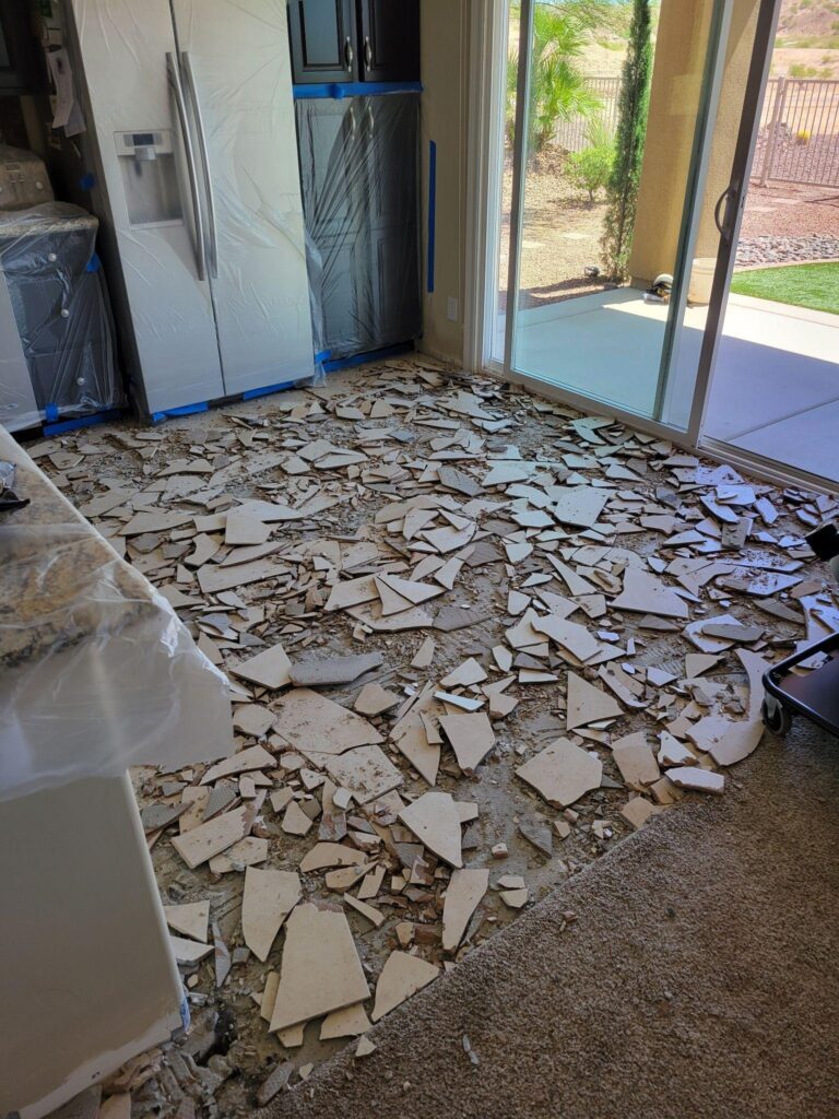 A kitchen with shattered glass on the floor beside an upright refrigerator