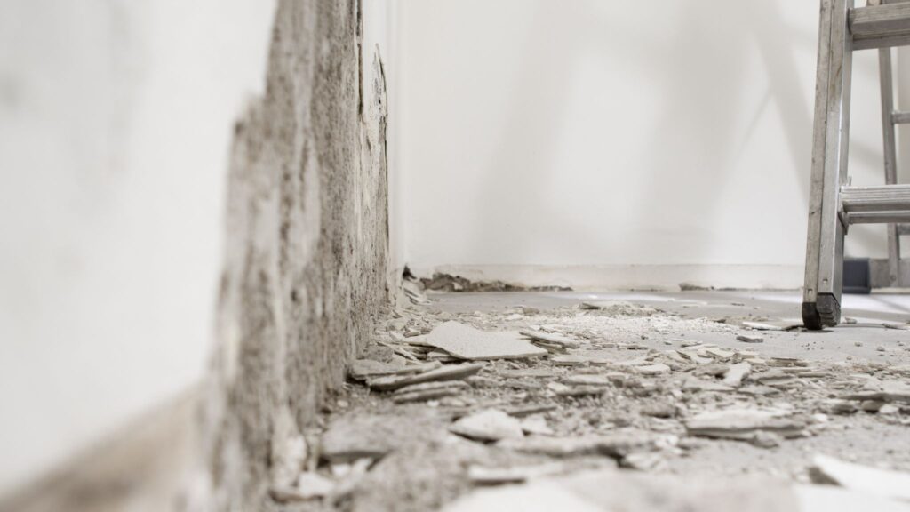 Chipped wall plaster and debris on the floor during room renovation.