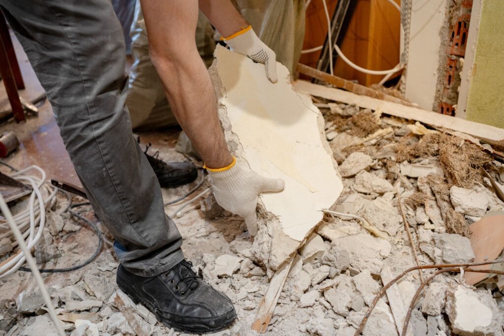 Construction worker holding a piece of broken drywall amid home renovation debris.