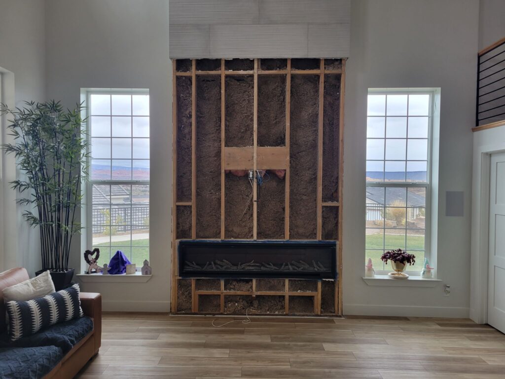 Exposed wooden framing and insulation around a modern electric fireplace during home remodeling.