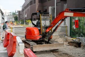 Compact orange excavator parked behind safety barriers at an urban road construction site.