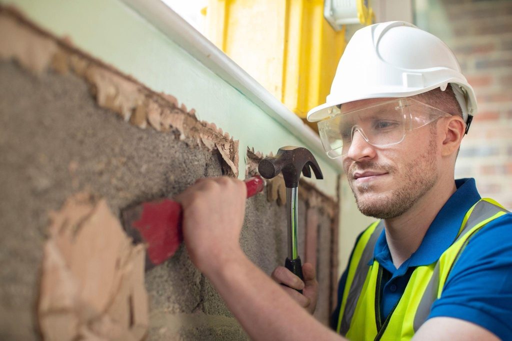 A man in a safety vest and hard hat is working on a wall showcasing construction safety practices